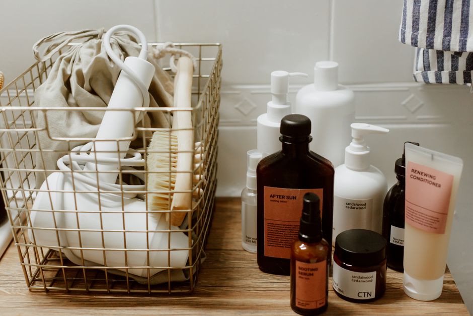 Imagem de uma coleção de produtos de cuidados pessoais e cosméticos organizados em uma superfície de madeira, com destaque para frascos, tubos e potes variados.