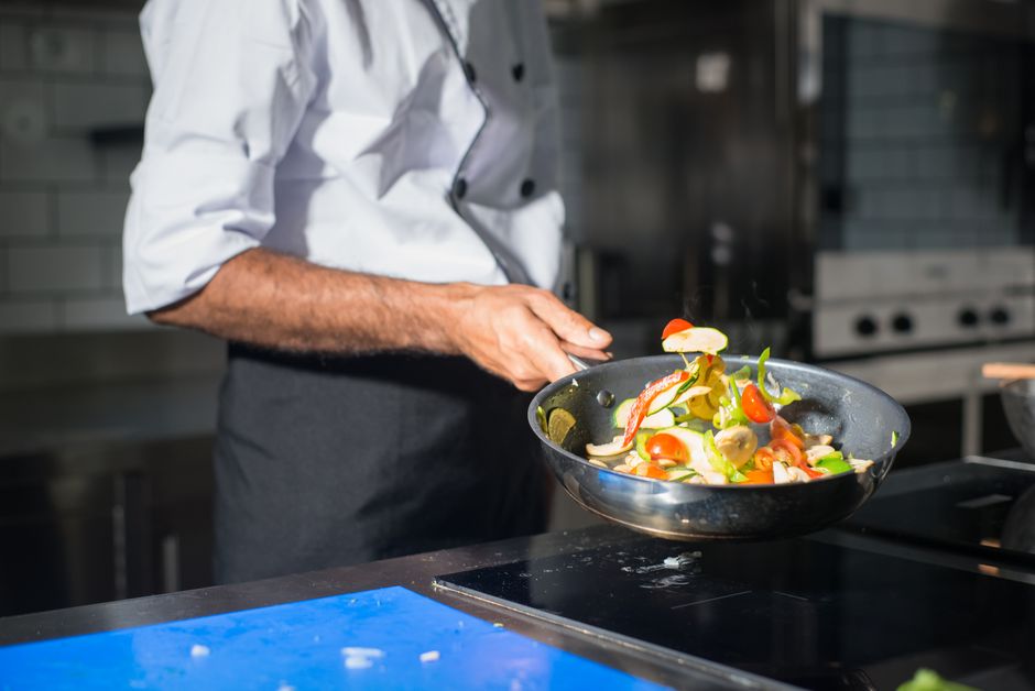 Imagem de um chef preparando um prato de salada fresca na cozinha, enfatizando culinária e gastronomia.