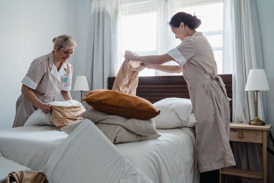 Duas profissionais de enfermagem organizando roupas de cama em um ambiente hospitalar ou de cuidado, destacando a rotina de higienização e arrumação na área da saúde.