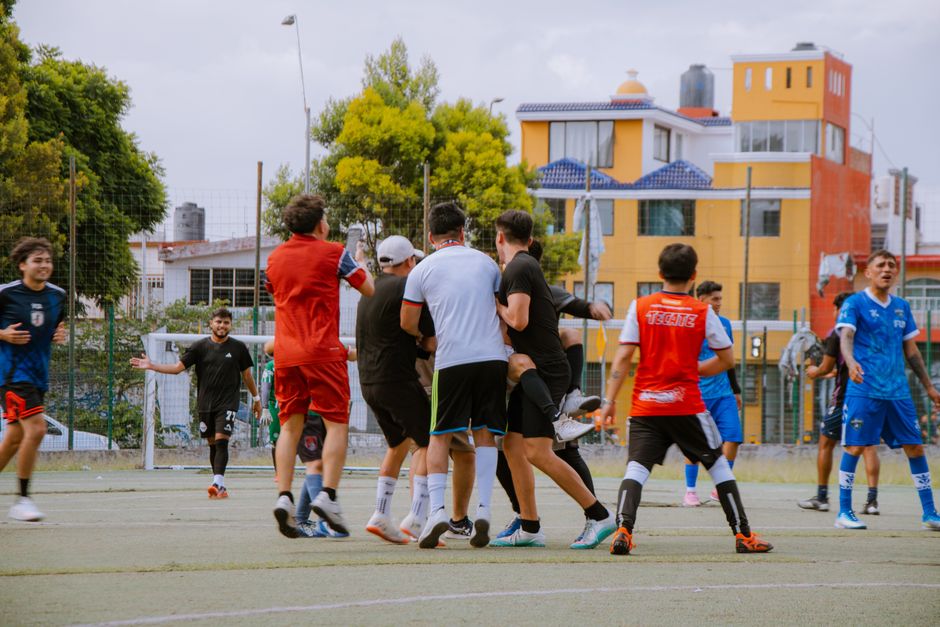 Grupo de jovens jogando futebol em um campo ao ar livre, destacando a prática esportiva e integração social.