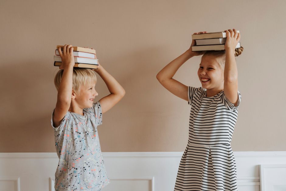 Duas crianças brincando de equilibrar livros na cabeça, explorando a diversão e a criatividade no ambiente doméstico.