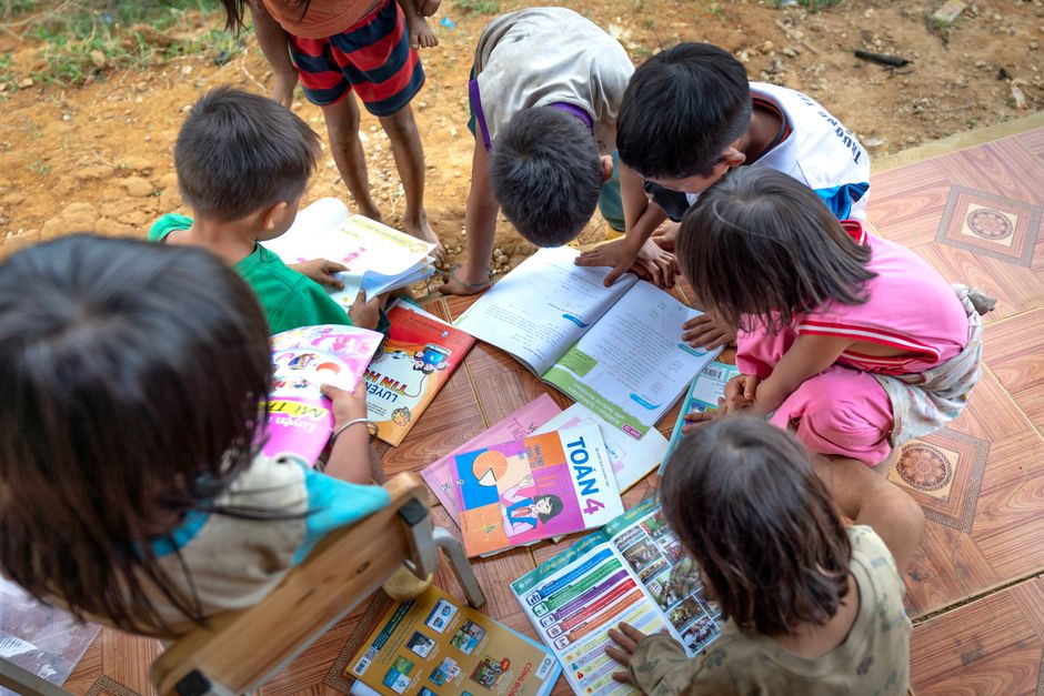 Grupo de crianças estudando ao ar livre, envolvendo materiais educativos e livros escolares.