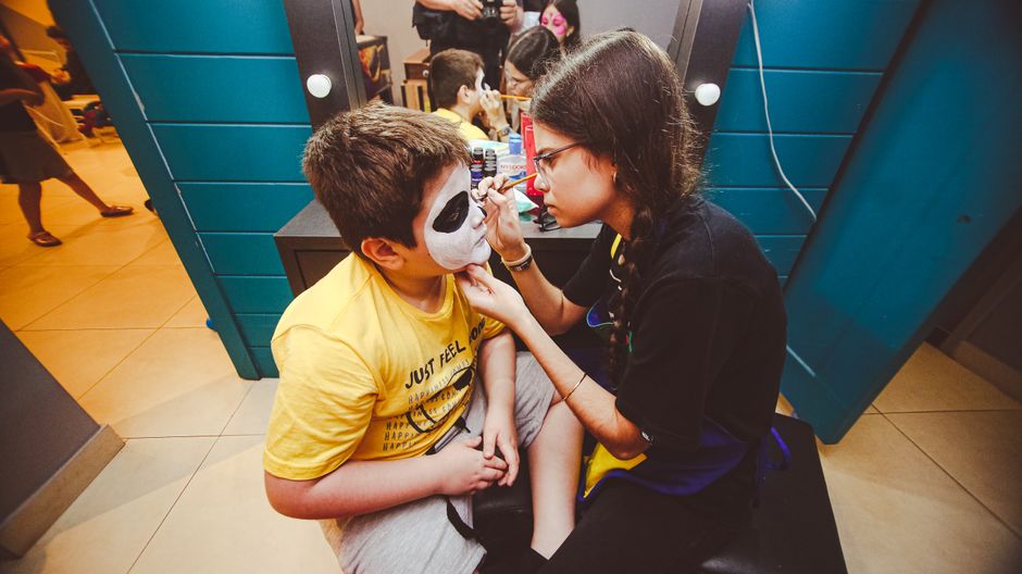 Criança se preparando para uma atividade de maquiagem facial em ambiente de evento infantil.