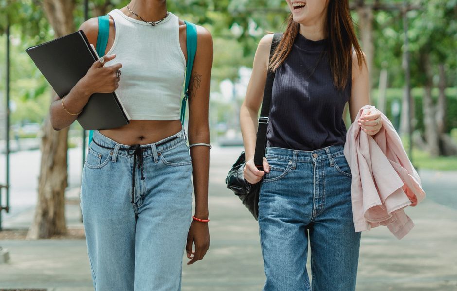 Duas jovens caminhando ao ar livre, compartilhando um momento de conversa descontraída, evidenciando amizade e lazer na natureza.