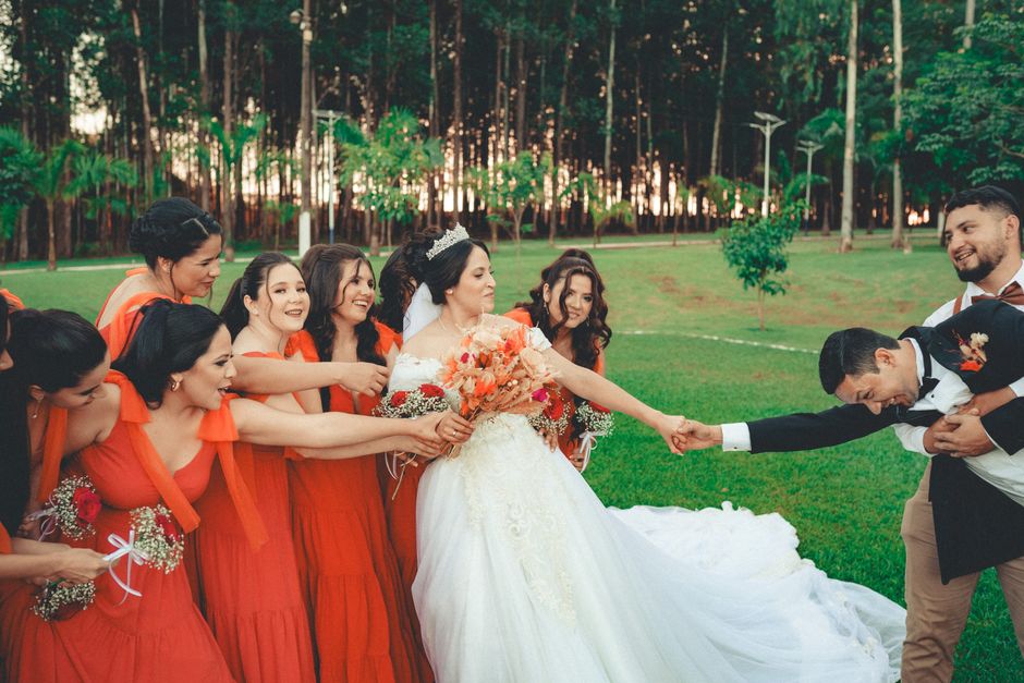 Casal de noivos sendo cercado pelas madrinhas e padrinhos em um cenário ao ar livre, simbolizando celebração de casamento.