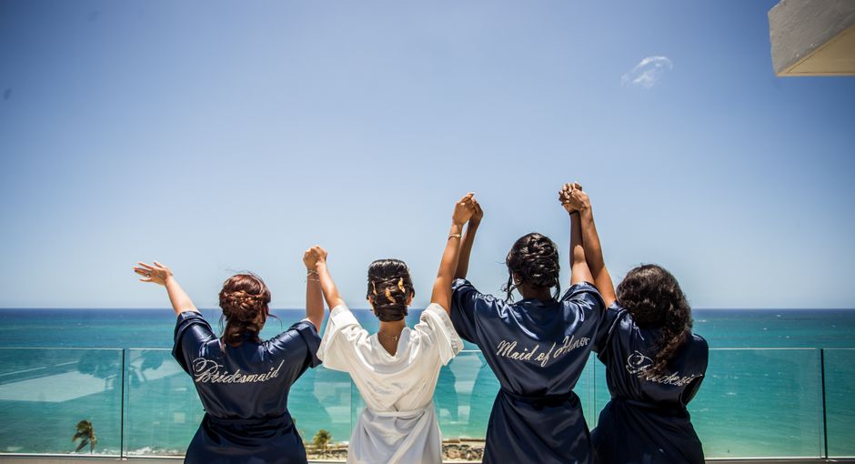 Grupo de mulheres celebrando na varanda com vista para o mar, simbolizando amizade e comemoração ao ar livre.
