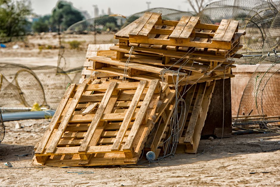 Imagem de uma pilha de pallets de madeira empilhados ao ar livre, possivelmente em um ambiente de armazenamento ou descarte de materiais recicláveis.