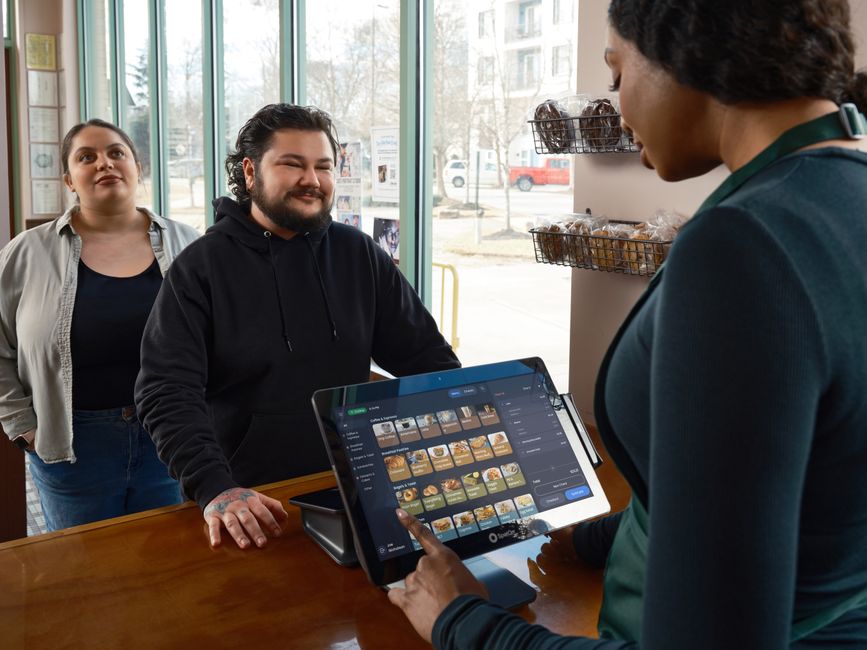 Clientes realizando pedido em um sistema digital no balcão de uma loja, com atendimento personalizado.