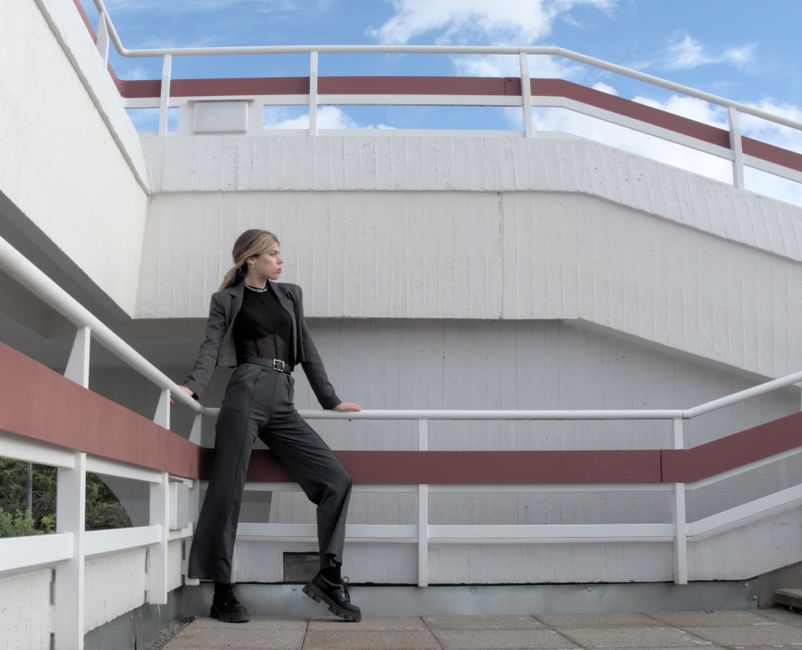 Mulher de roupa de trabalho posando em uma estrutura de concreto com céu azul ao fundo, transmitindo confiança e profissionalismo.