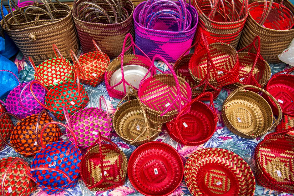 Imagem de cestas artesanais coloridas em uma feira de artesanato, destacando o acabamento em palha e o uso de cores vibrantes.