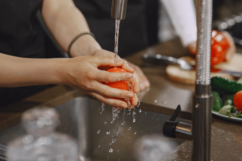 Pessoa lavando legumes na cozinha, mostrando a importância da higiene na preparação de alimentos.