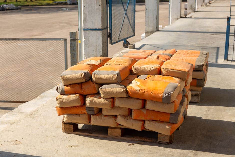 Imagem de sacos de cimento empilhados em um pátio de obra, destacando o tema de construção civil e materiais de construção.