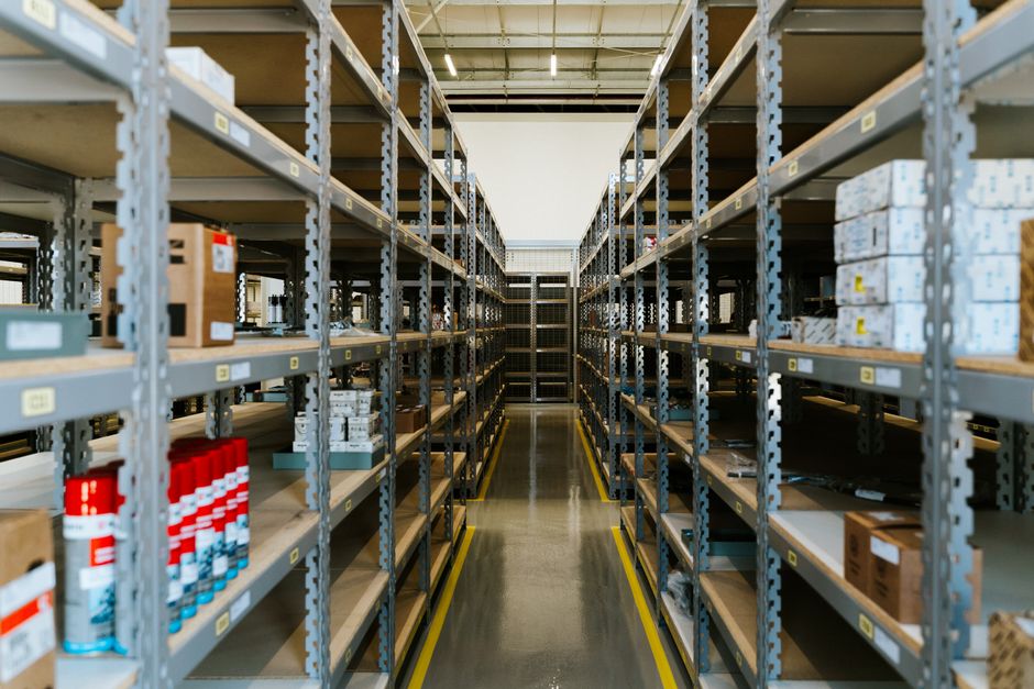 Imagem de um armazém organizado com várias prateleiras cheias de caixas e produtos para gestão de estoque empresarial.