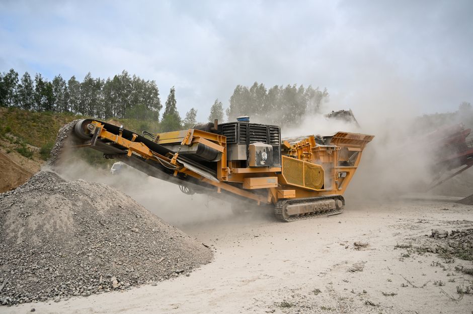 Caminhão de britagem operando em uma obra de construção, gerando poeira e movimento na área.