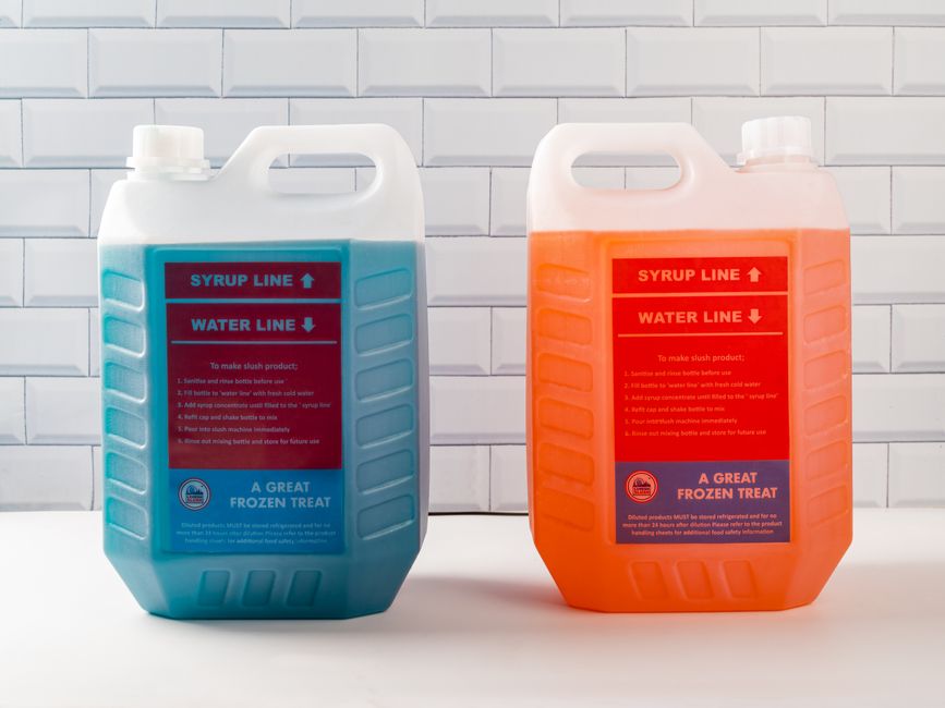 Imagem de dois grandes tanques de sorvete de cores diferentes, um azul e outro laranja, usados na produção de sorvetes congelados, sobre fundo de parede de azulejos brancos.