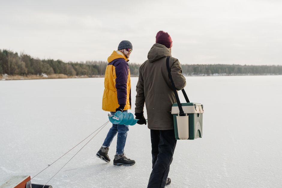Dois homens caminhando sobre uma superfície congelada, possivelmente para pescar ou explorar a natureza no inverno.