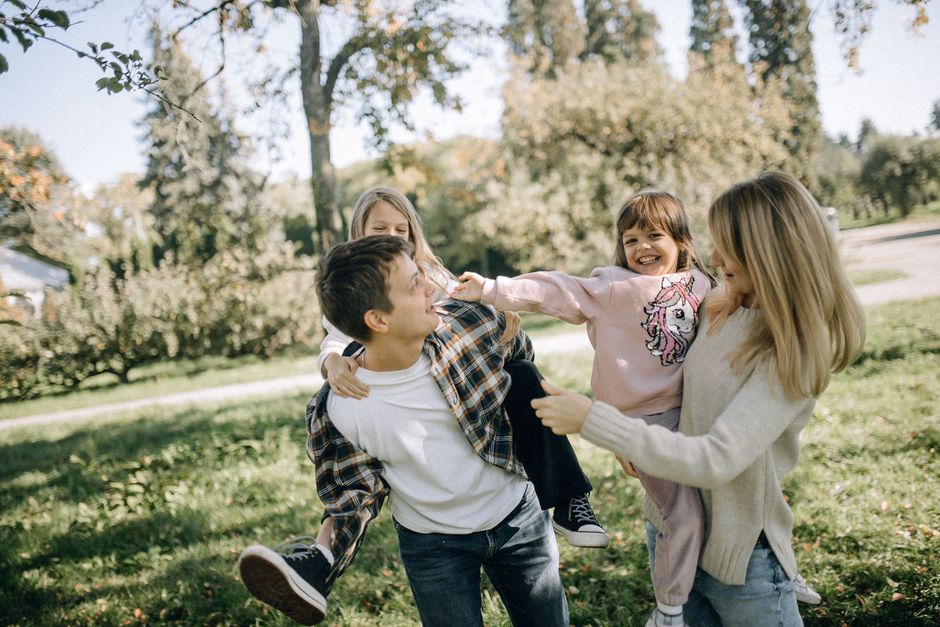 Família brincando e sorrindo ao ar livre, promovendo momentos de diversão e união.