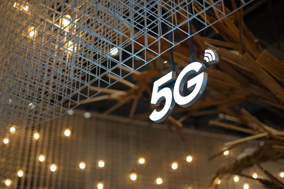 Sinalização luminosa exibindo um símbolo de conexão 5G em um ambiente moderno com estrutura de metal e iluminação ambiente acolhedora.