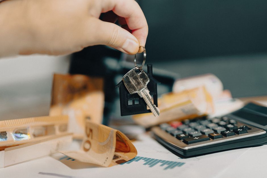 Pessoa usando uma chave para abrir uma casa ao lado de elementos relacionados a finanças e planejamento imobiliário.