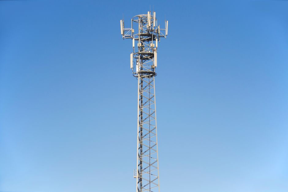 Imagem de uma torre de transmissão de sinais de telecomunicações contra um céu azul claro, simbolizando conectividade e tecnologia.