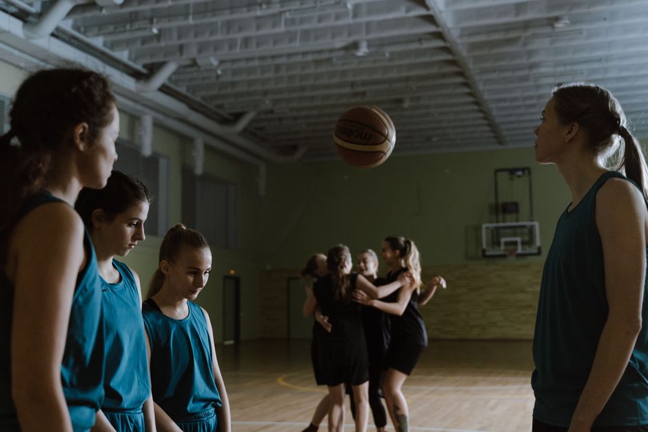 Grupo de jogadoras de basquete treinando em uma quadra coberta, com foco na preparação técnica e tática do esporte.