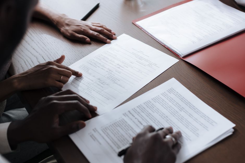 Pessoas revisando documentos importantes em uma reunião de negócios ou assinatura de contratos, com foco em aspectos de gestão empresarial e planejamento financeiro.