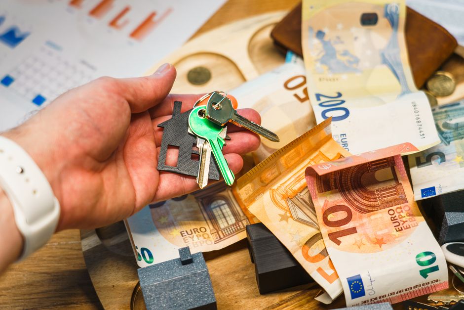 Imagem de uma pessoa segurando uma chave de casa junto com um conjunto de dinheiro e documentos, simbolizando financiamento imobiliário ou compra de imóvel.