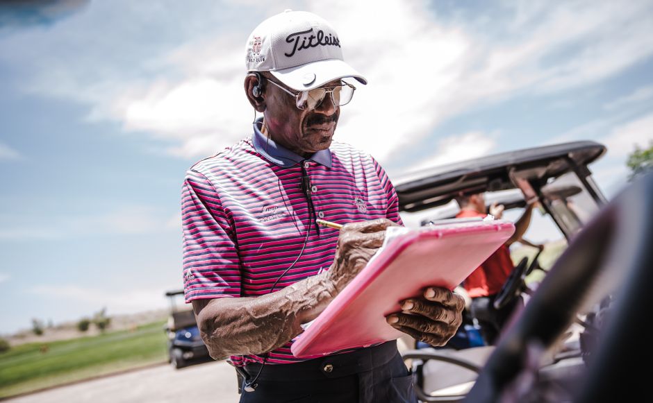 Homem profissional de golfe anotando informações em uma prancheta ao ar livre, relacionado a gestão esportiva ou preparação de esporte.