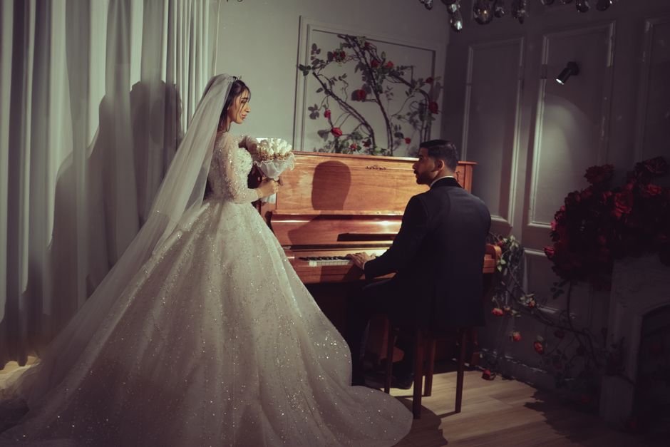 Casal de noivos em um momento romântico, onde a noiva segura um buquê e o noivo toca piano, simbolizando amor e celebração do casamento.