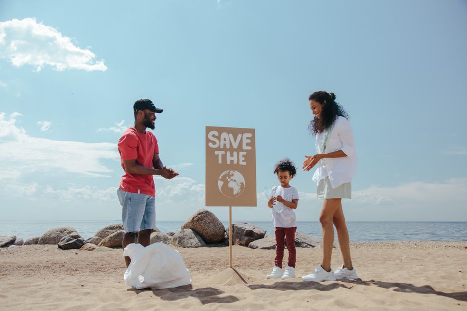 Família participando de uma ação de conscientização ambiental na praia, com um cartaz de protesto sobre a importância da preservação do planeta.