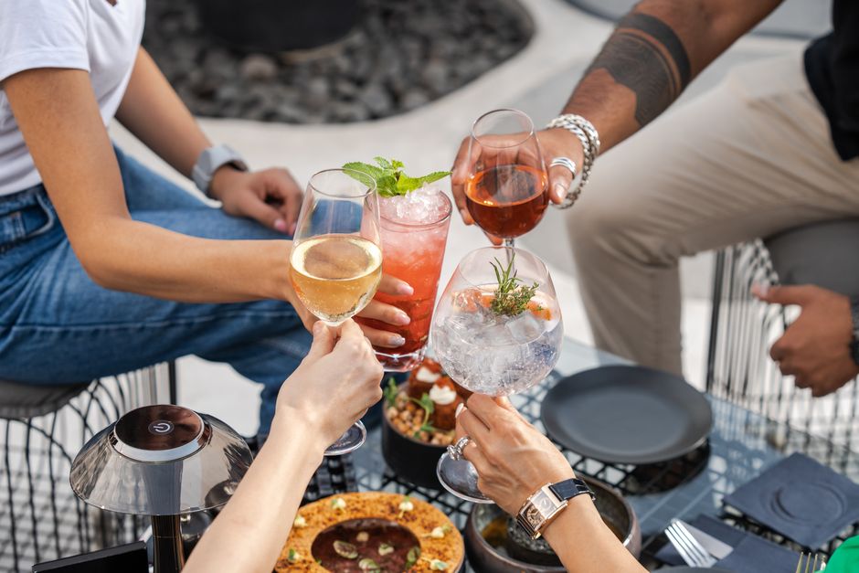 Pessoas brindando com drinks coloridos durante uma reunião social ao ar livre, celebrando momentos especiais com amigos.