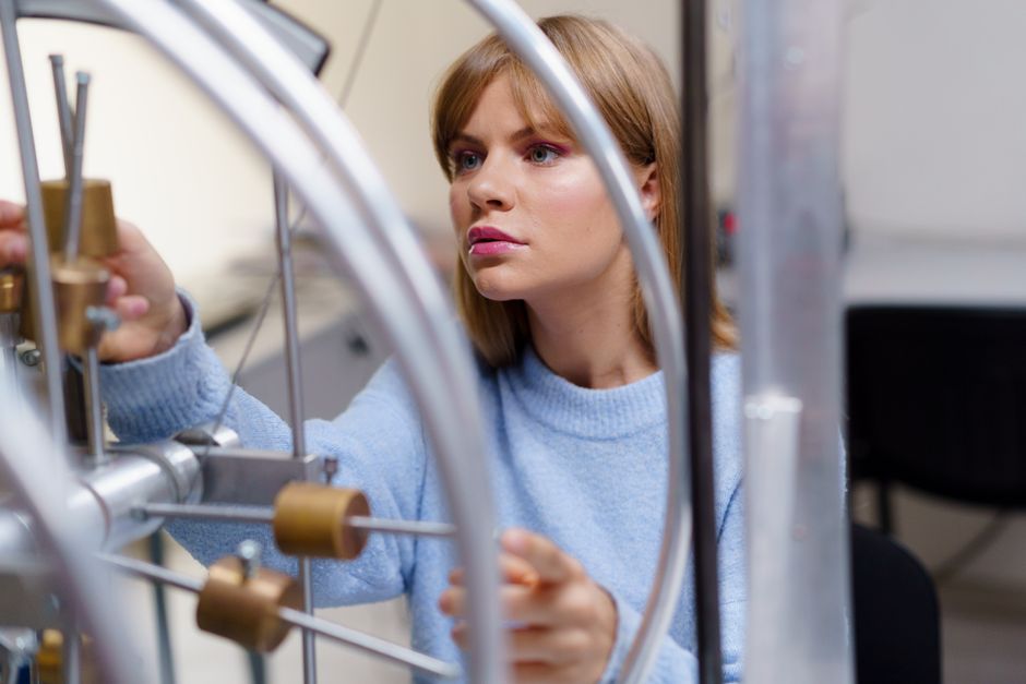 Mulher trabalhando em um laboratório de tecnologia ou engenharia, ajustando um dispositivo científico ou equipamento de pesquisa.