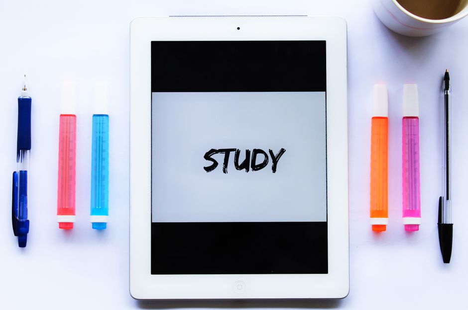 Imagem de um tablet com a palavra 'STUDY' na tela, rodeado por canetas e marcadores coloridos, simbolizando o foco em estudo e aprendizado.