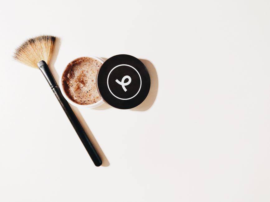 Imagem representando cuidados com a pele ou beleza, com pó compacto, pincel de maquiagem e embalagem de produto em fundo branco.