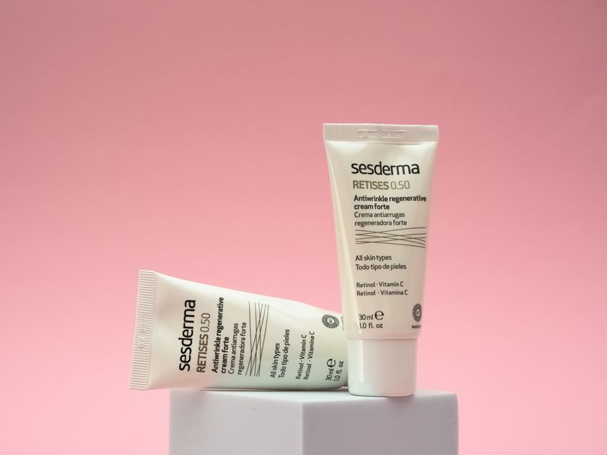 Imagem de dois tubos de creme anti-idade contra rugas em um fundo rosa suave, destacando cuidados com a pele e beleza.