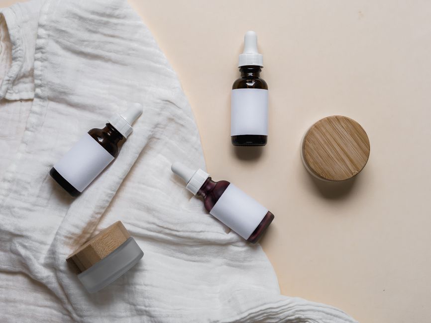 Imagem de frascos de óleo essencial e um creme em ambiente clean, sugestiva de cuidados com a saúde e bem-estar natural.