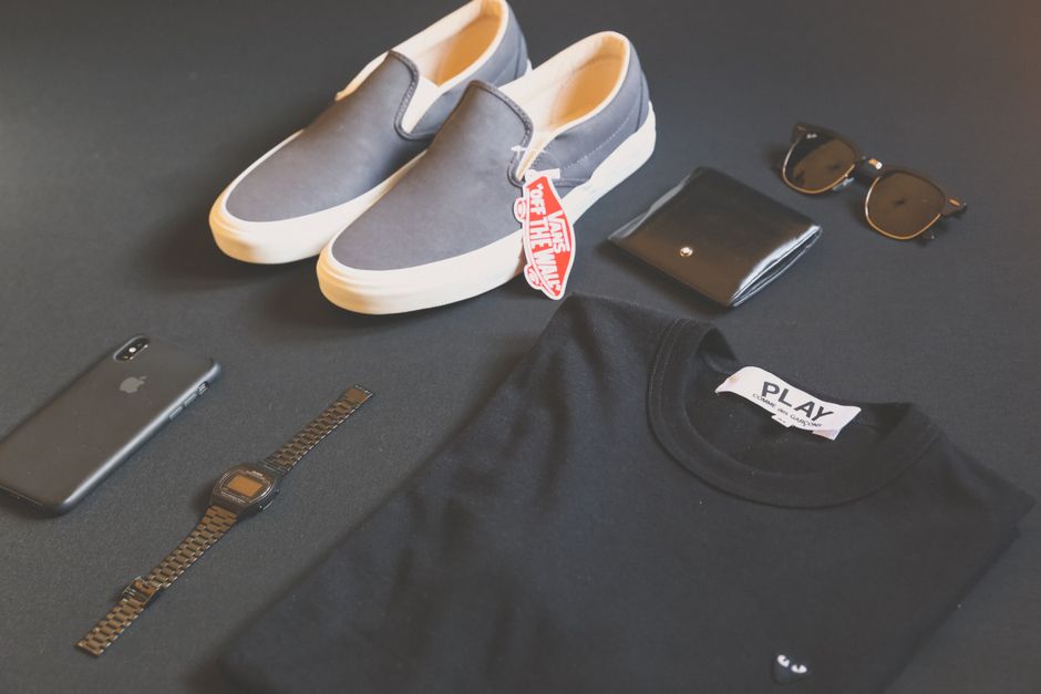 Coleção de itens de estilo casual e acessíveis, incluindo tênis, óculos de sol, carteira, relógio, celular e camisa preta, ideal para mostrar moda urbana ou looks descomplicados.