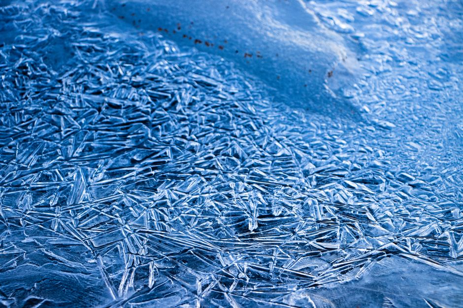 Imagem de uma superfície de gelo com cristais de gelo formando desenhos complexos, ideal para ilustrar temas como inverno, clima frio ou preservação ambiental.