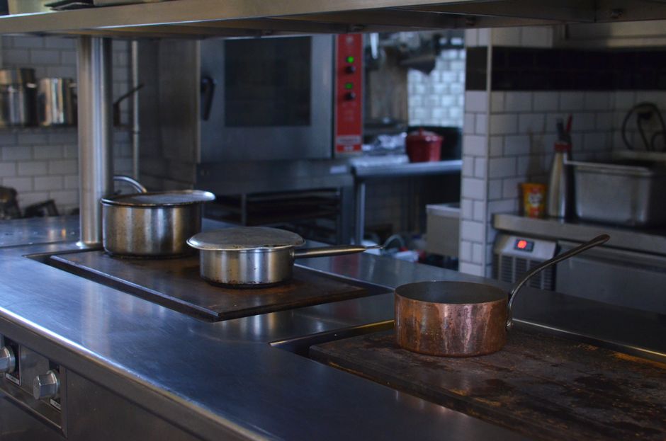 Uma cozinha industrial com utensílios de cozimento em aço e cobre, evidenciando um ambiente de culinária profissional ou de restaurante.