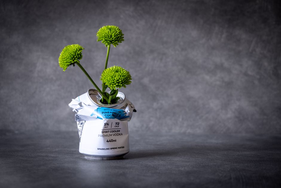 Uma lata de refrigerante reciclada transformada em vaso com flores verdes, simbolizando sustentabilidade e criatividade.
