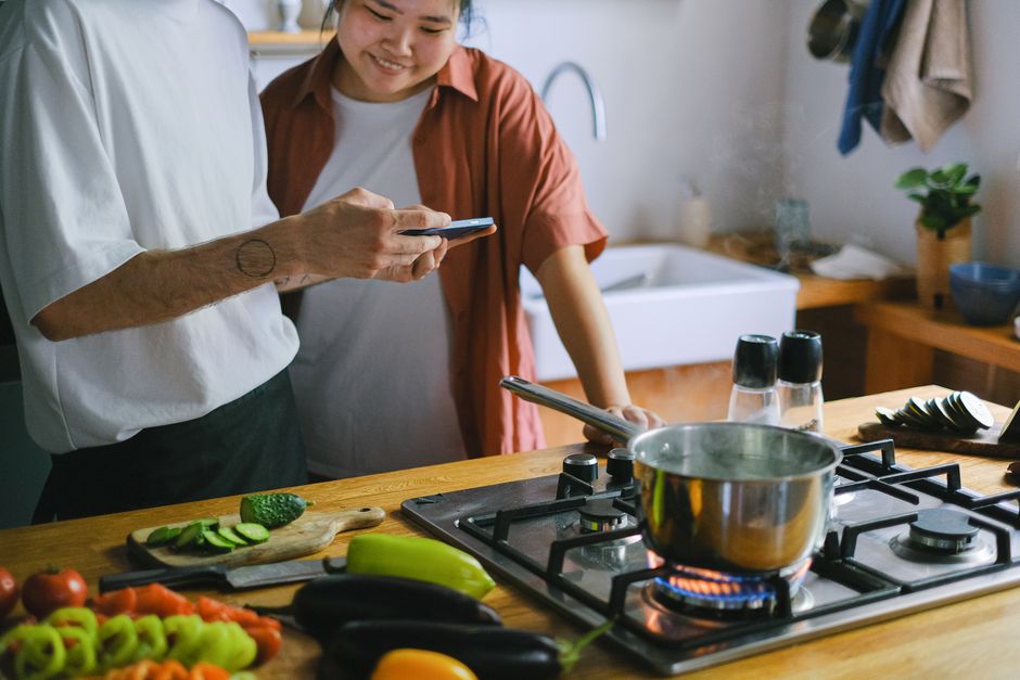 Duas pessoas interagindo em uma cozinha moderna, compartilhando um momento de conversa enquanto usam smartphones, evidenciando o tema de convivência e tecnologia no ambiente doméstico.