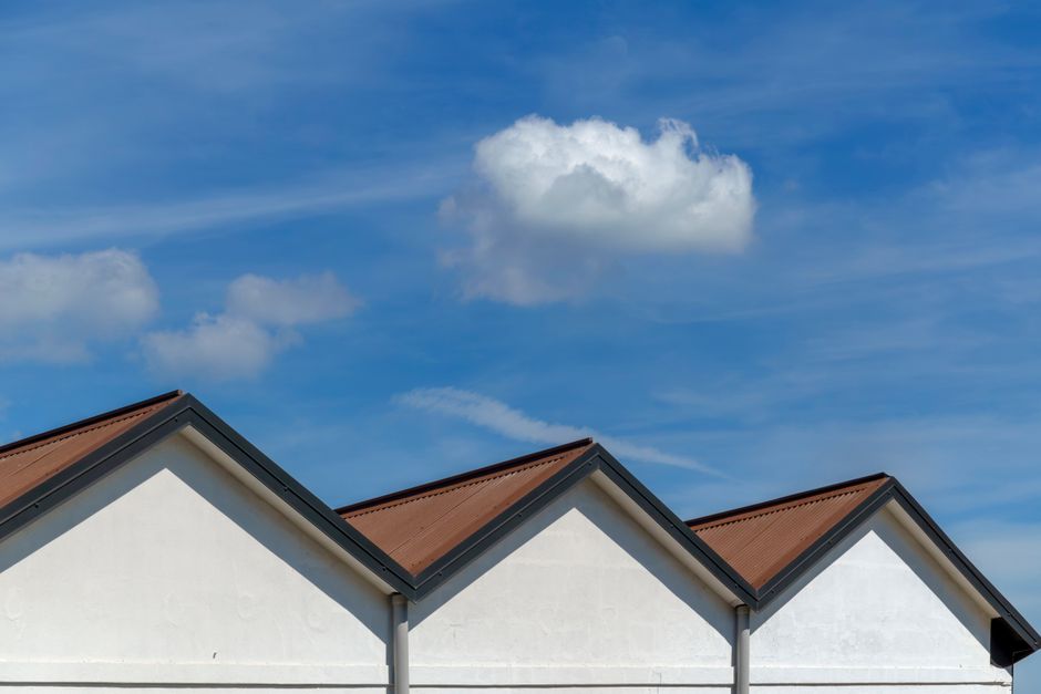 Imagem de telhados residenciais sob um céu azul com nuvens, simbolizando estabilidade e proteção. 