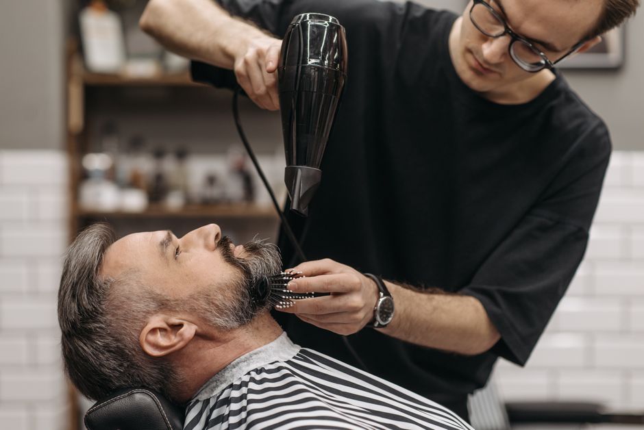 Barbeiro aparando a barba de um cliente em um ambiente de barbearia moderno, focando na atenção ao detalhe e cuidado pessoal.