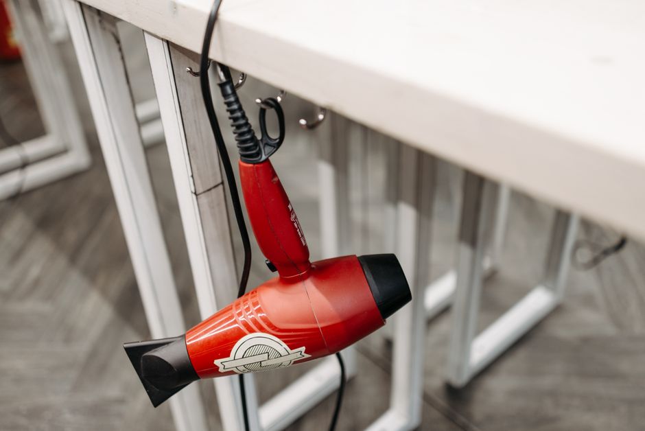Secador de cabelo vermelho pendurado sob uma bancada de trabalho, sugerindo um ambiente de estética ou cabeleireiro.