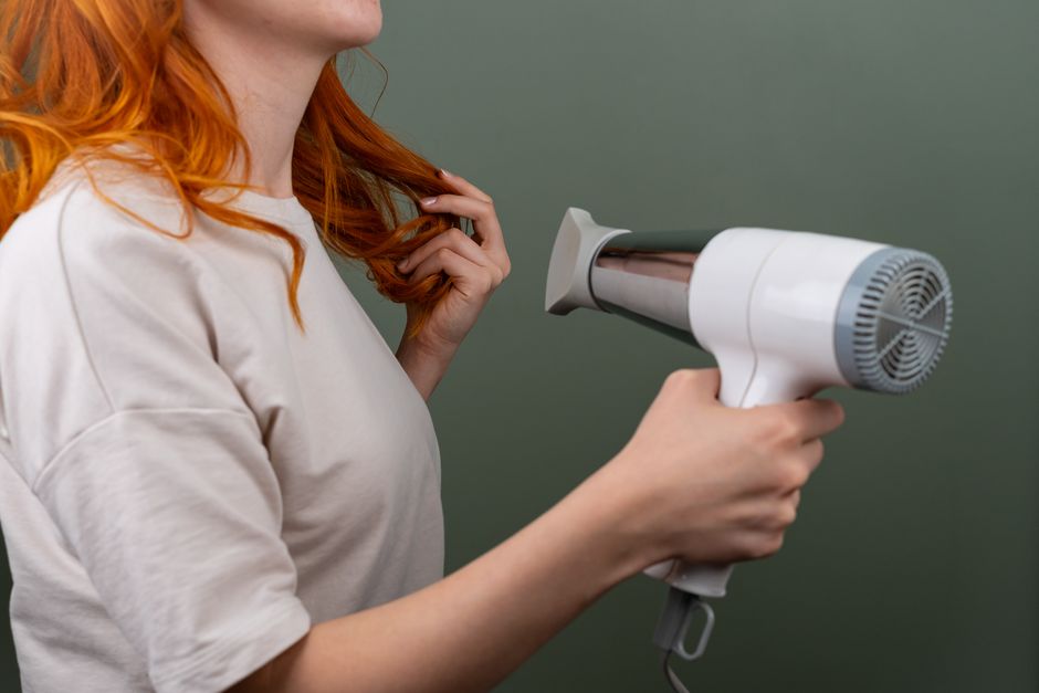 Mulher com cabelo ruivo usando um secador de cabelo, preparando-se para o dia a dia ou cuidado pessoal.