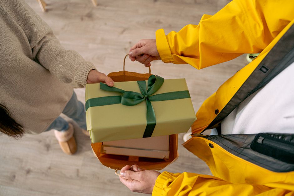 Pessoa entregando um presente embrulhado, simbolizando troca de presentes ou homenagem em um ambiente de interação social.
