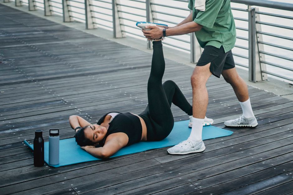 Imagem de uma pessoa realizando exercícios físicos ao ar livre com a ajuda de um parceiro, simbolizando saúde e bem-estar.