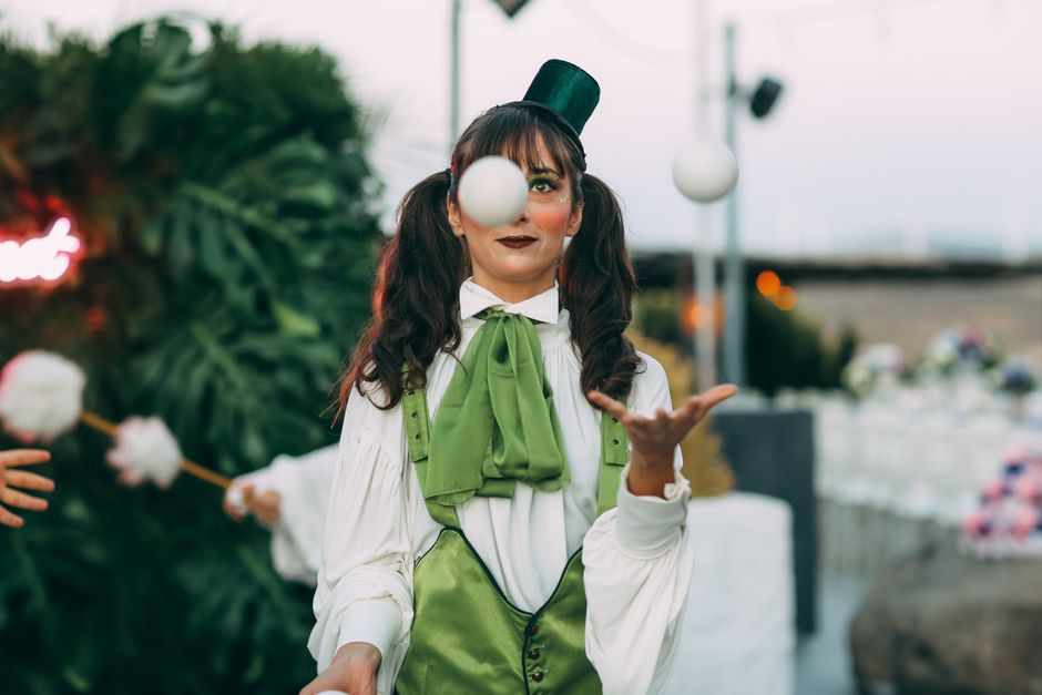 Pessoa vestida de palhaço brincando com uma bola em ambiente ao ar livre, promovendo diversão e entretenimento.
