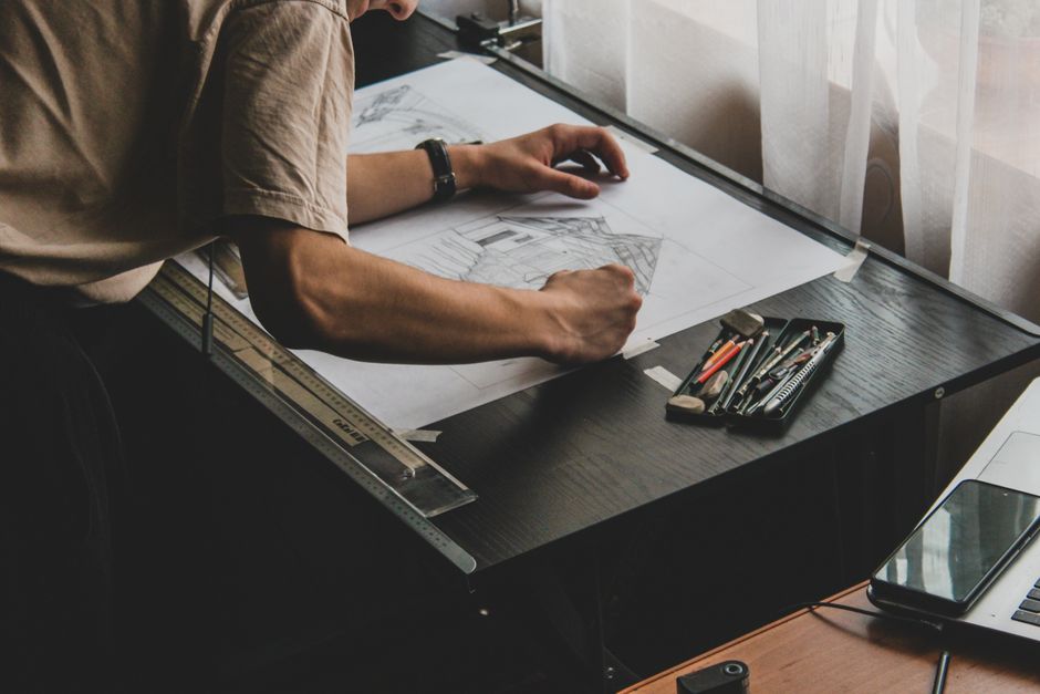 Profissional trabalhando em projetos arquitetônicos ou de design em um ambiente de escritório com luz natural.