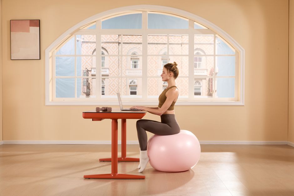 Mulher praticando exercícios de alongamento ou pilates enquanto trabalha em um ambiente ensolarado com grande janela de arco.